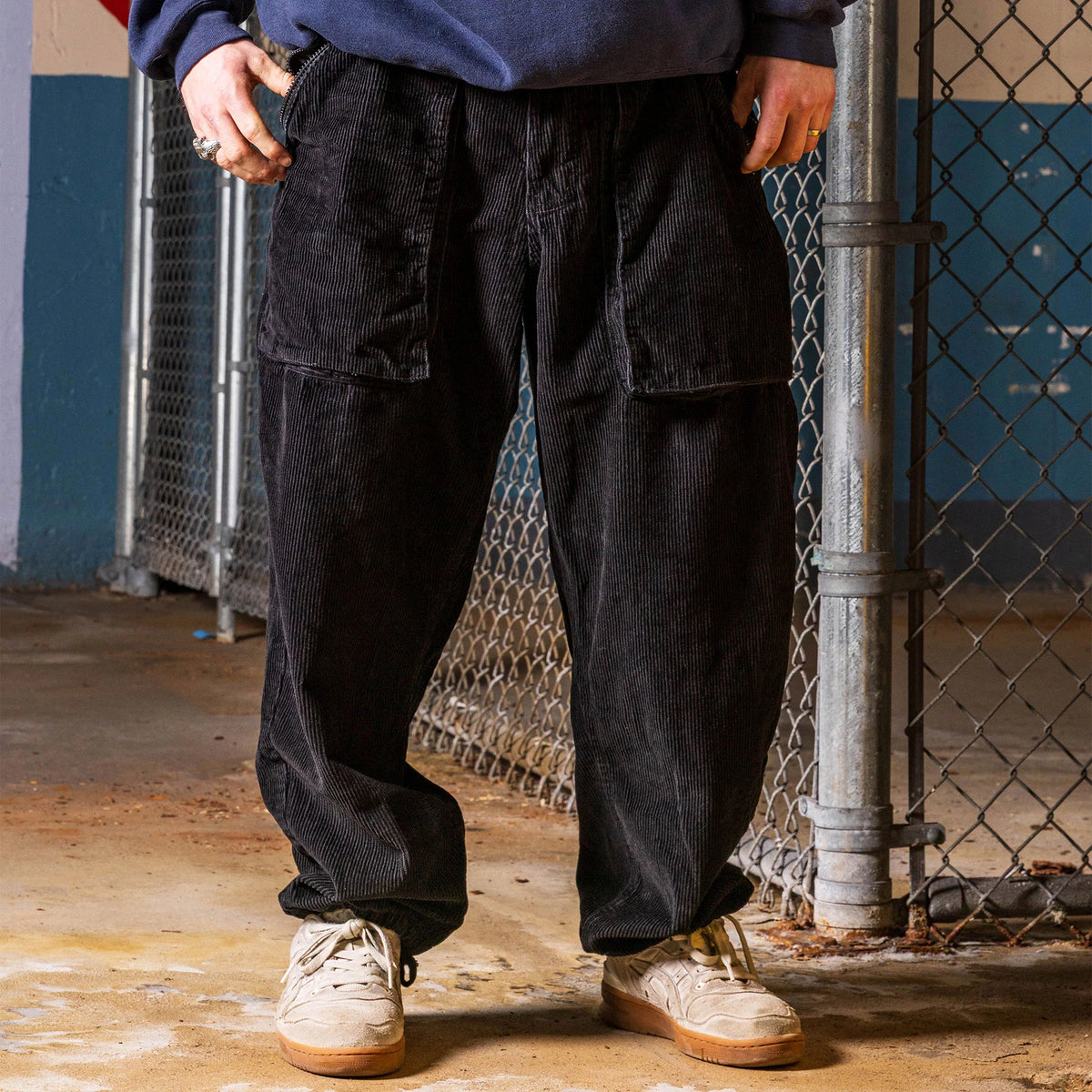 Snack Mic Check Corduroy Pants Black on model by chainlink fence
